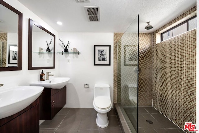 bathroom with a textured ceiling, vanity, a tile shower, and tile patterned flooring