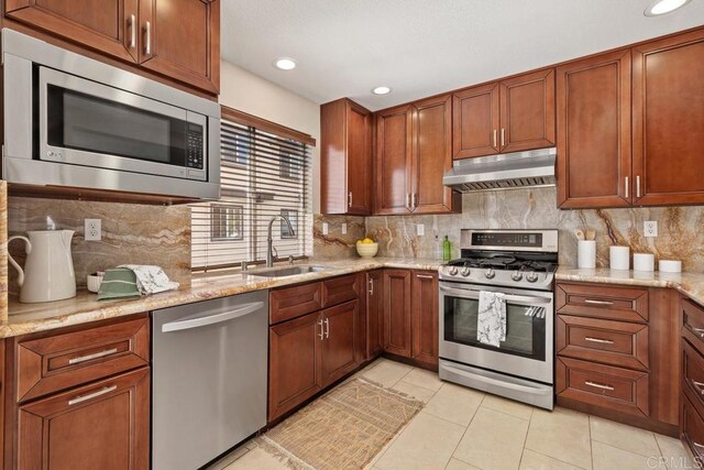 kitchen with light stone countertops, stainless steel appliances, sink, backsplash, and light tile patterned floors