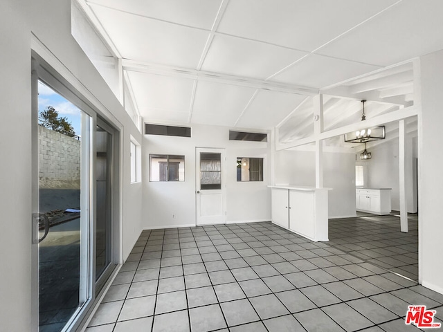 empty room with plenty of natural light, tile patterned flooring, lofted ceiling, and an inviting chandelier