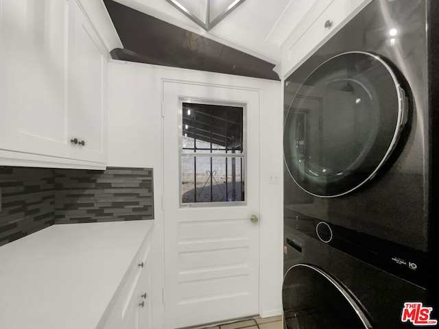 clothes washing area featuring stacked washing maching and dryer, cabinets, and light tile patterned flooring