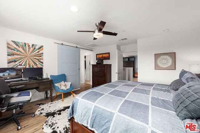 bedroom with ceiling fan, wood-type flooring, and a barn door