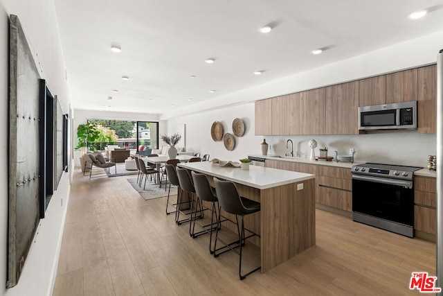 kitchen with light wood-type flooring, a kitchen bar, appliances with stainless steel finishes, and a center island