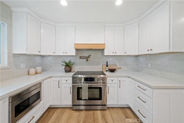 kitchen featuring light wood-type flooring, backsplash, stainless steel appliances, and white cabinetry