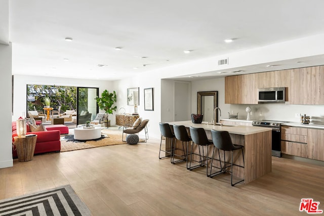 kitchen with appliances with stainless steel finishes, sink, a kitchen island with sink, a breakfast bar, and light hardwood / wood-style flooring