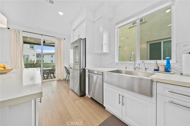 kitchen with light wood finished floors, a sink, decorative backsplash, stainless steel appliances, and white cabinetry