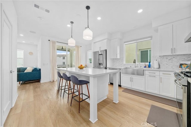 kitchen featuring hanging light fixtures, a center island, white cabinets, and appliances with stainless steel finishes