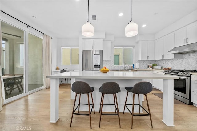 kitchen with white cabinetry, under cabinet range hood, light wood-style flooring, and appliances with stainless steel finishes