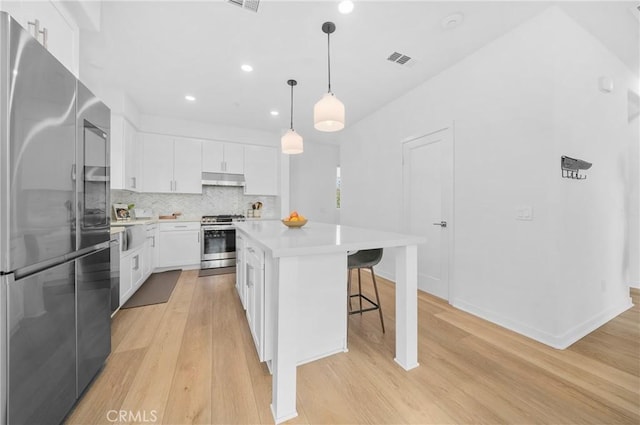 kitchen with a kitchen island, appliances with stainless steel finishes, white cabinetry, hanging light fixtures, and light hardwood / wood-style floors