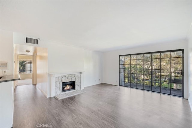 unfurnished living room featuring a high end fireplace, a healthy amount of sunlight, and light hardwood / wood-style flooring