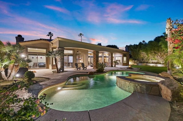 pool at dusk with a patio area and an in ground hot tub