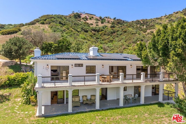 rear view of property featuring a yard, an outdoor living space, solar panels, and a patio