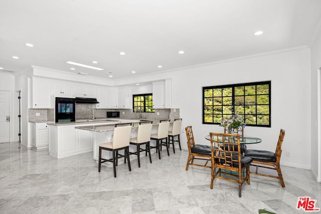 kitchen with a kitchen island, a breakfast bar, white cabinetry, ornamental molding, and light stone counters