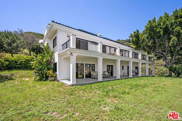 back of property with a yard, a balcony, and a patio