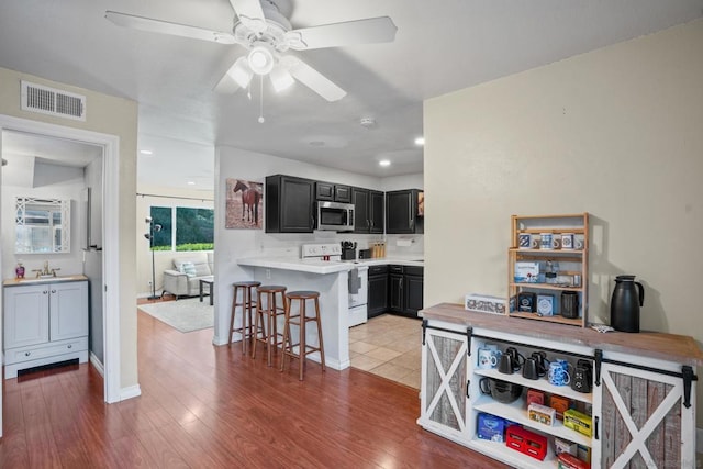 kitchen featuring electric stove, kitchen peninsula, ceiling fan, light hardwood / wood-style flooring, and a breakfast bar area