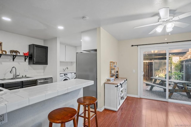 kitchen with appliances with stainless steel finishes, tile counters, a kitchen bar, sink, and kitchen peninsula