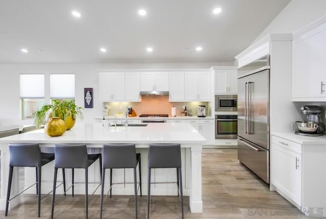 kitchen with a breakfast bar area, white cabinets, and built in appliances