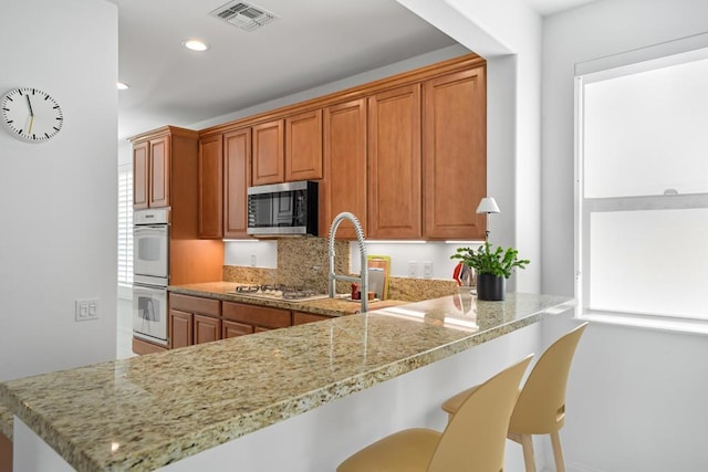 kitchen with light stone counters, stainless steel appliances, a kitchen breakfast bar, and kitchen peninsula