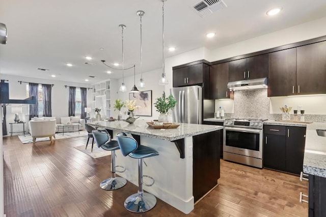 kitchen featuring pendant lighting, appliances with stainless steel finishes, a kitchen island, a breakfast bar, and dark brown cabinets