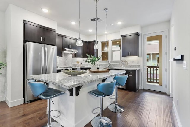 kitchen with stainless steel refrigerator, a kitchen breakfast bar, hanging light fixtures, light stone countertops, and a center island