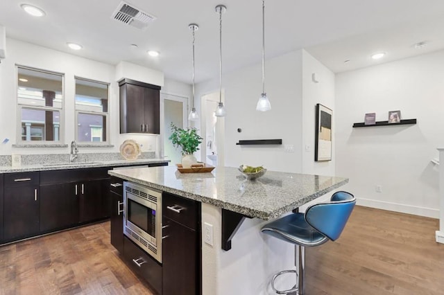 kitchen with stainless steel microwave, dark hardwood / wood-style floors, a kitchen island, sink, and dark brown cabinetry