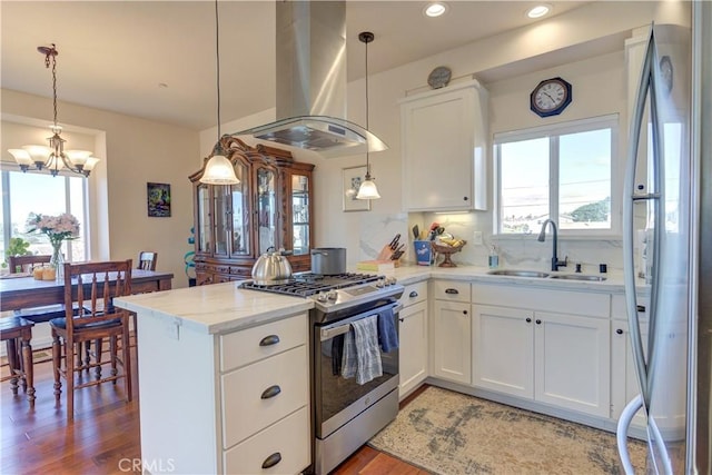 kitchen featuring white cabinets, decorative light fixtures, stainless steel appliances, kitchen peninsula, and island range hood