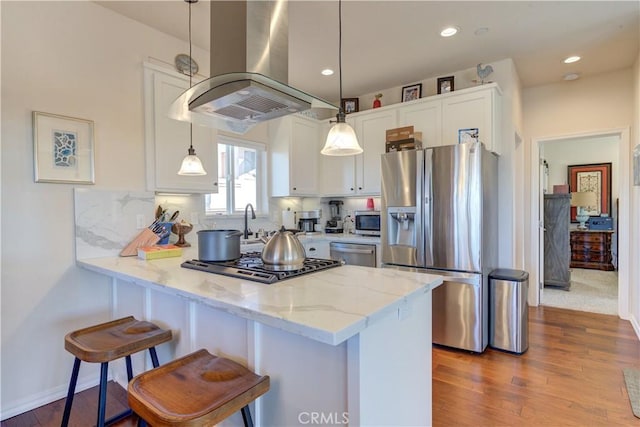 kitchen with light stone countertops, pendant lighting, appliances with stainless steel finishes, white cabinetry, and island exhaust hood