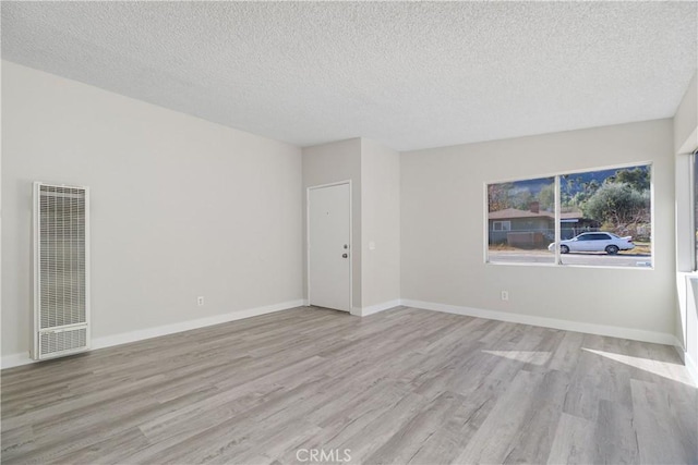 empty room featuring a textured ceiling, a heating unit, wood finished floors, and baseboards