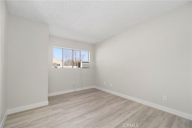 empty room featuring cooling unit, a textured ceiling, baseboards, and wood finished floors