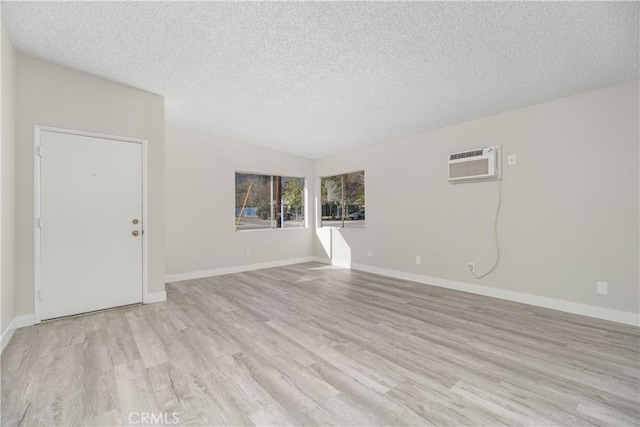 empty room with an AC wall unit, baseboards, a textured ceiling, and light wood finished floors