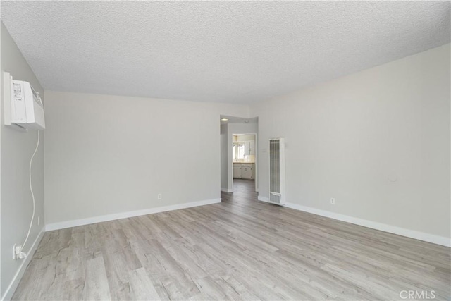 empty room with a textured ceiling, light wood finished floors, and baseboards