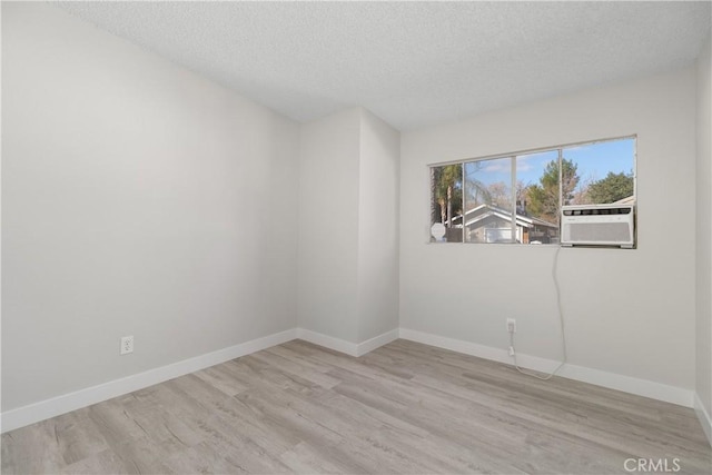 empty room with cooling unit, a textured ceiling, baseboards, and wood finished floors