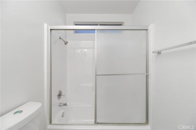 bathroom featuring toilet and combined bath / shower with glass door