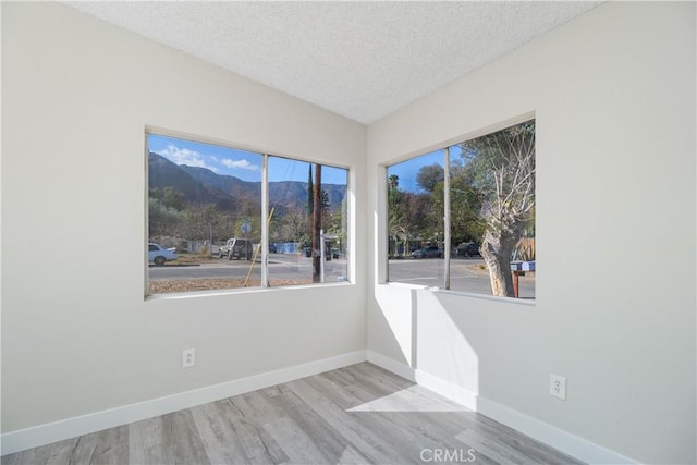 empty room featuring a mountain view, a textured ceiling, baseboards, and wood finished floors