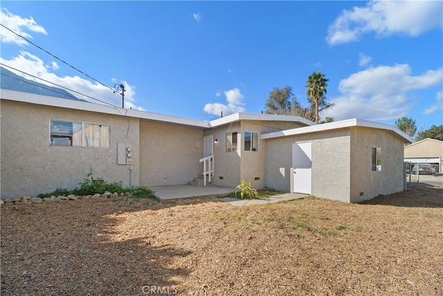 back of house with crawl space, a patio area, a lawn, and stucco siding