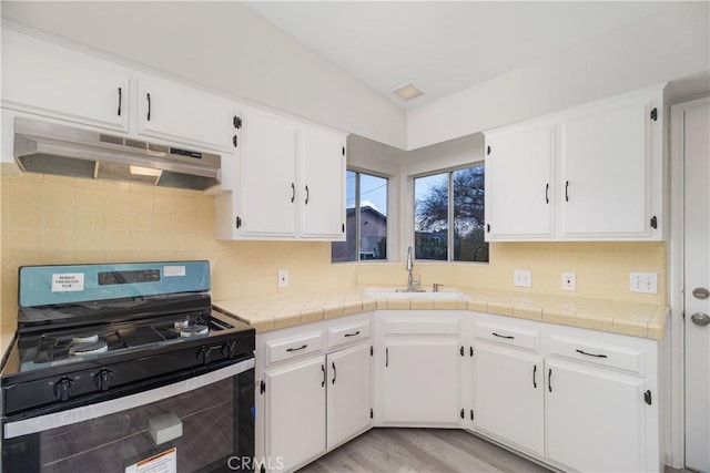 kitchen with white cabinets, decorative backsplash, gas range oven, under cabinet range hood, and a sink