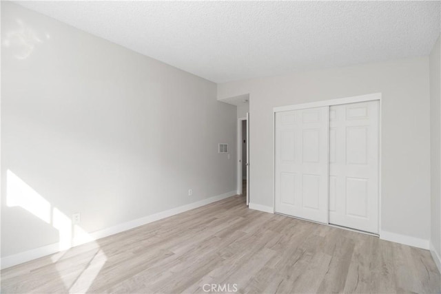 unfurnished bedroom with a closet, baseboards, a textured ceiling, and light wood finished floors