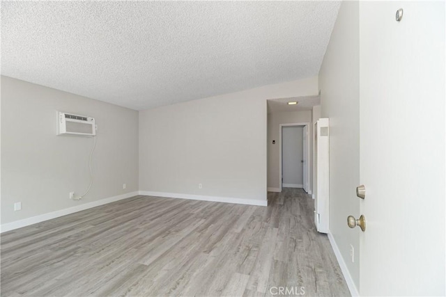 unfurnished room featuring baseboards, a wall mounted AC, a textured ceiling, and light wood-style floors