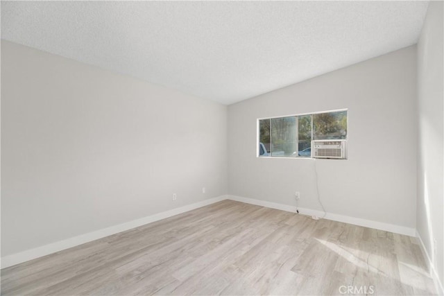 empty room featuring light wood-type flooring, baseboards, and a textured ceiling