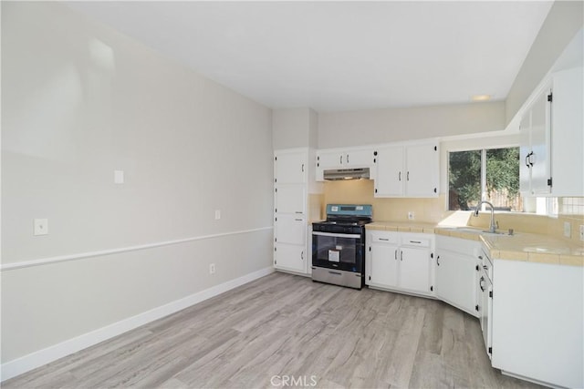 kitchen with under cabinet range hood, a sink, white cabinets, tile counters, and stainless steel gas stove