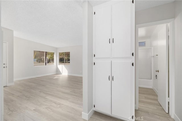 hall with light wood-style floors, baseboards, and a textured ceiling