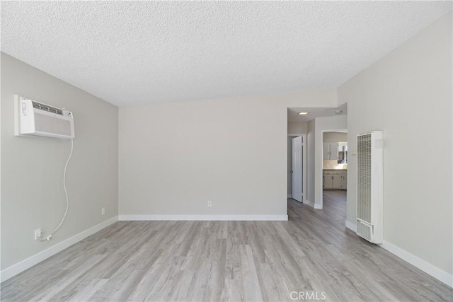 spare room with light wood-style flooring, baseboards, a textured ceiling, and a wall mounted air conditioner