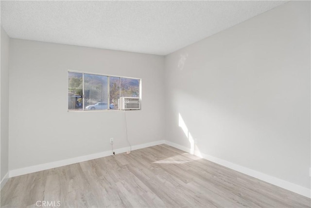 empty room with cooling unit, a textured ceiling, baseboards, and wood finished floors