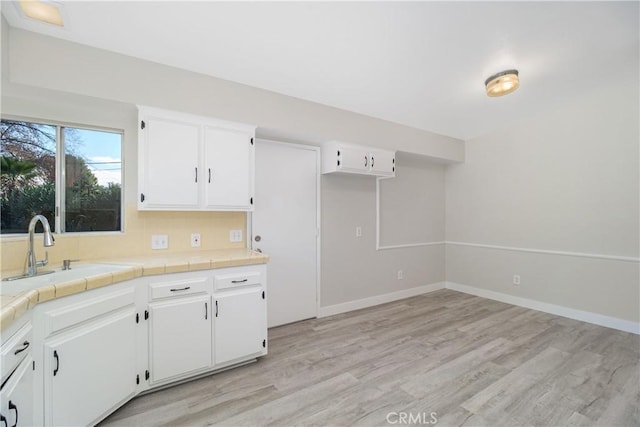 kitchen with tile countertops, light wood-style flooring, a sink, and white cabinetry