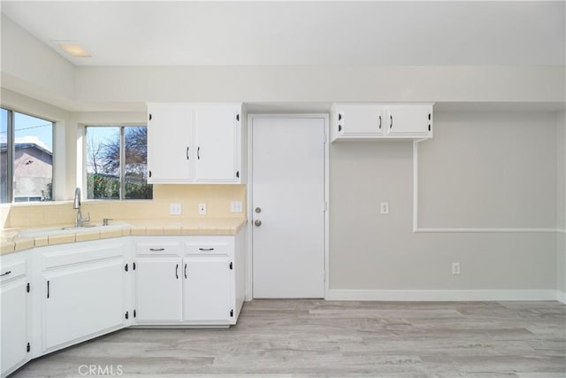 kitchen with tile counters, white cabinets, a sink, and light wood-style flooring