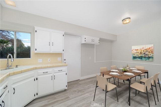 kitchen with tile counters, white cabinets, a sink, and light wood finished floors