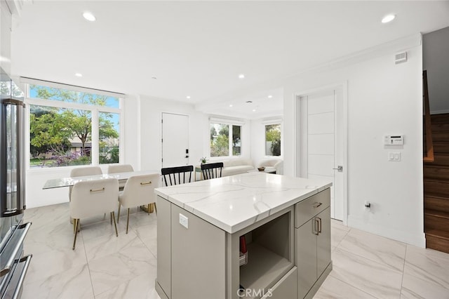 kitchen with gray cabinetry, high quality fridge, light stone countertops, ornamental molding, and a center island