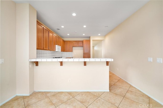 kitchen featuring decorative backsplash, kitchen peninsula, tile countertops, light tile patterned floors, and a breakfast bar area