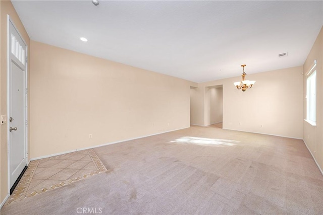 unfurnished room featuring light carpet and a chandelier