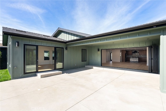 rear view of property with concrete driveway, an attached carport, board and batten siding, and a patio