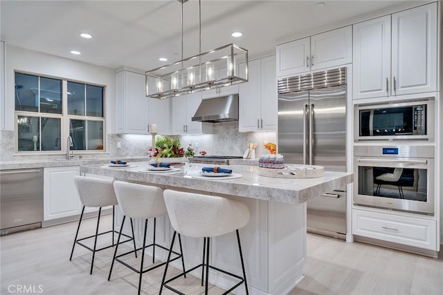 kitchen featuring white cabinetry, hanging light fixtures, built in appliances, and a kitchen island